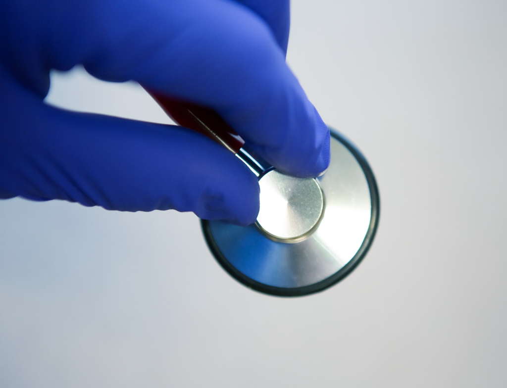 A hand wearing examination gloves holding a stethescope