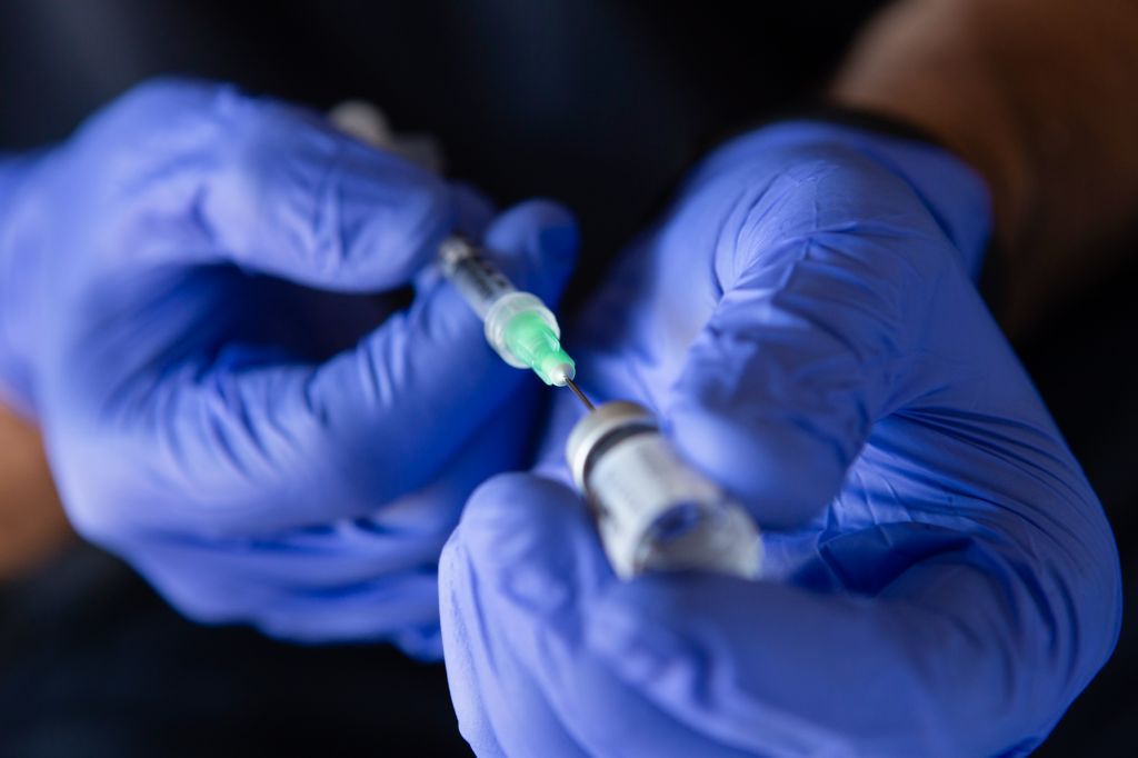 An EMS provider wearing examination gloves preparing filling a needle and syringe with medication