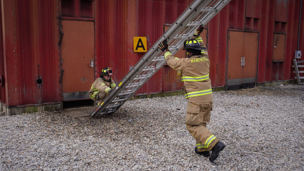 Two firefighters raising an extension ladder using the flat raise technique.