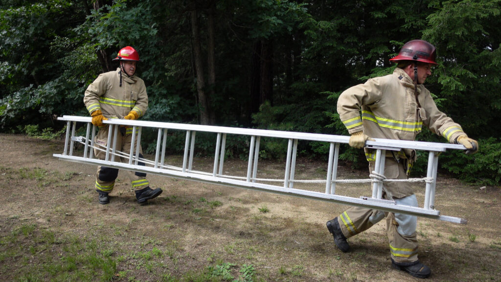 Two firefighters work together to move an extension ladder in a suitcase fashion.
