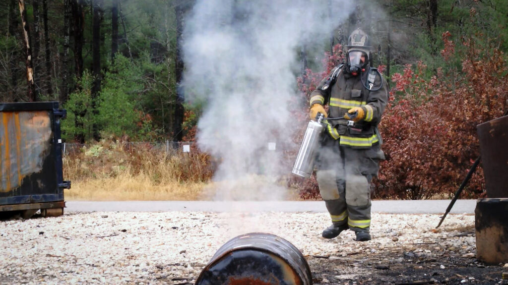 A firefighter in full PPE and SCBA extinguishes an outside fire with an APW extinguisher.