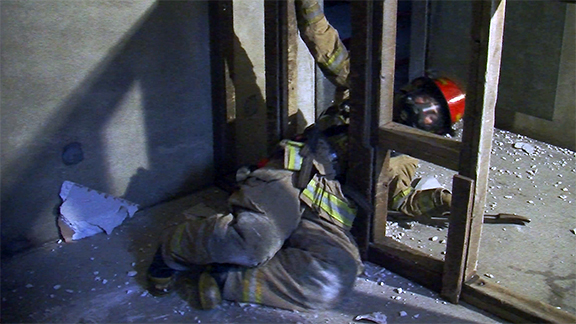 A firefighter moving from one space to another between wall studs.