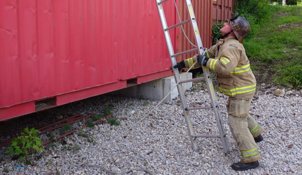 A firefighter rolling an extension ladder into position
