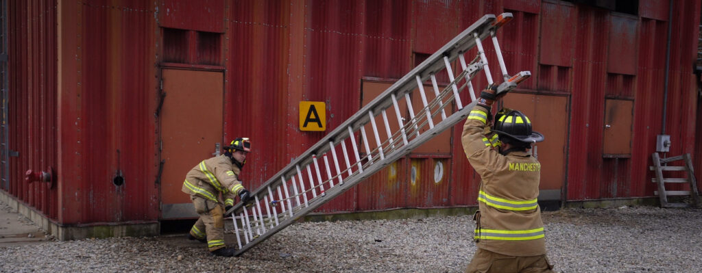 Two firefighters raising an extension ladder using the beam raise technique.