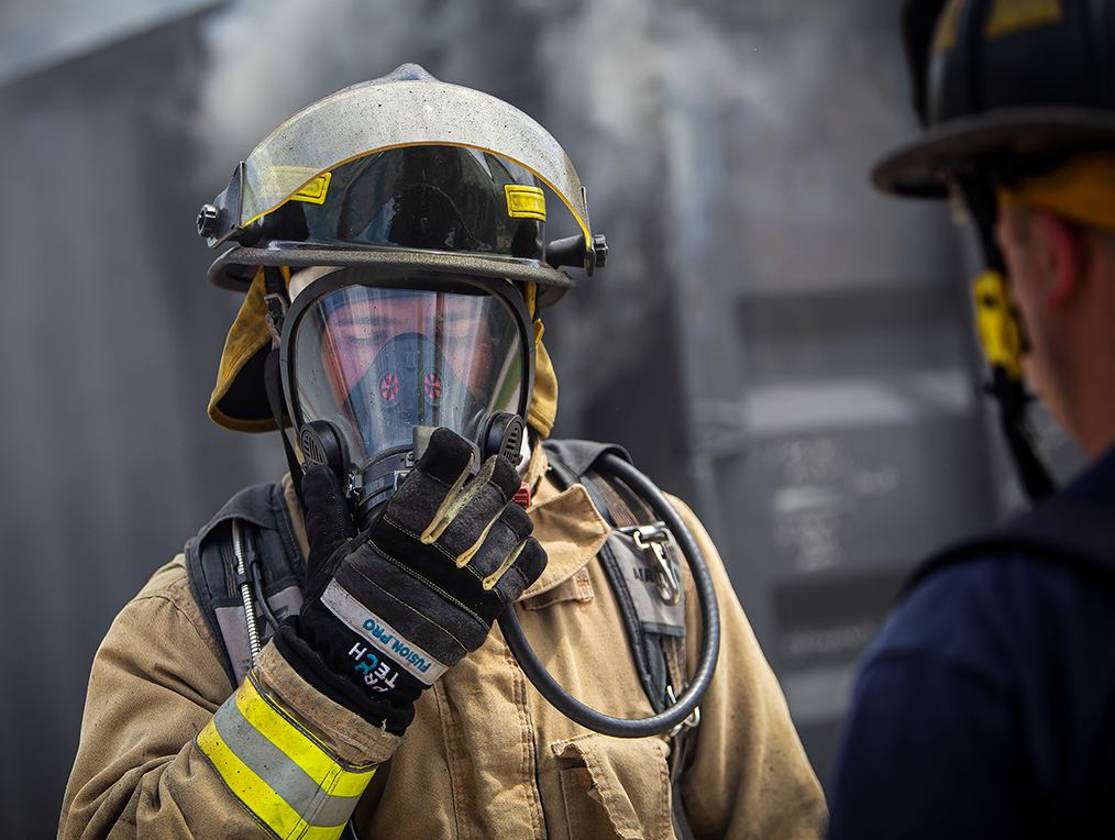 A firefighter removes regulator from SCBA facepiece while instructor watches